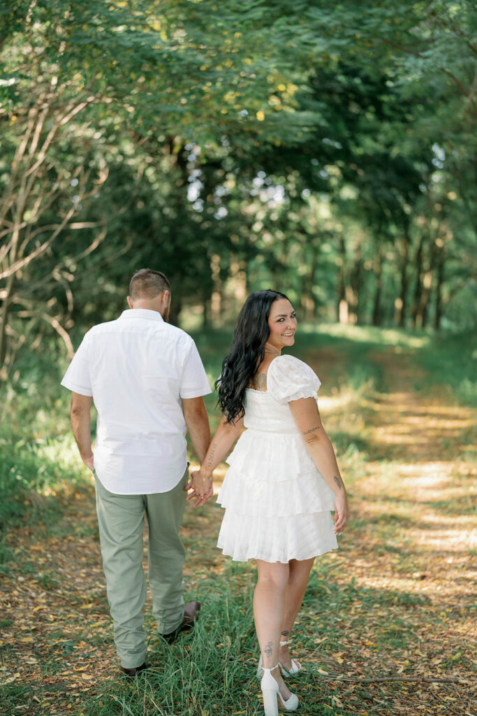 Couple walking hand in hand through a wooded path during their Michigan engagement session
