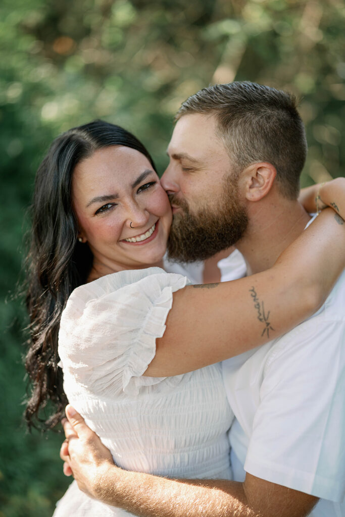 Couple hugging and smiling in soft natural light during their outdoor Michigan engagement photos