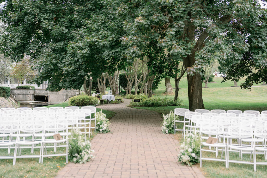 Outdoor ceremony aisle at Wellers Weddings lined with brick pathways and white chairs surrounded by greenery