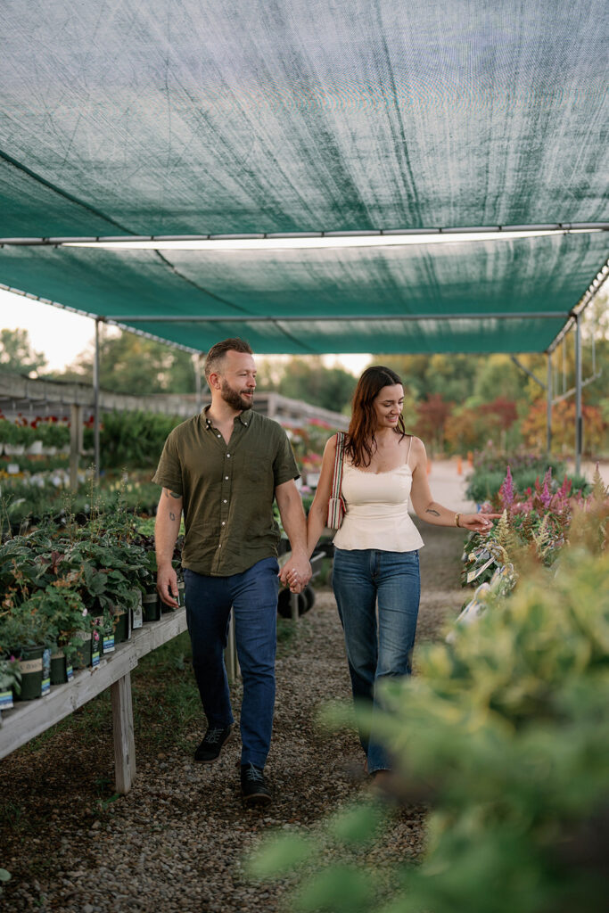 Engaged couple walking together under greenhouse shade structure at Sawyer Garden Center, relaxed outdoor engagement session.