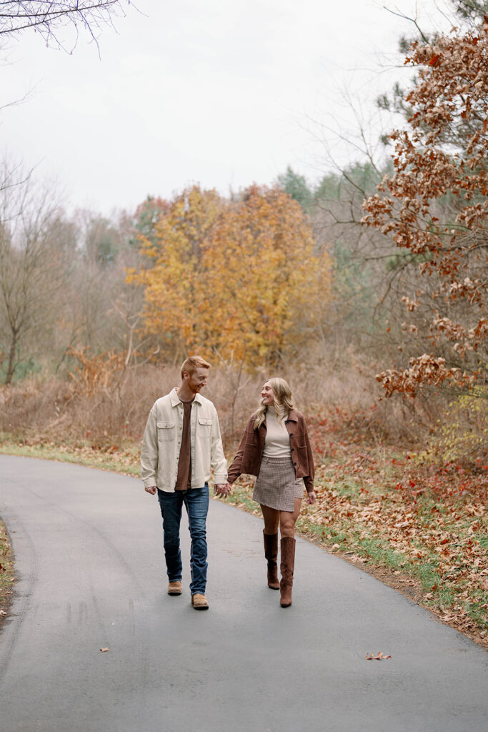 Engaged couple walking down a quiet road with fall leaves in the background, Michigan autumn engagement photos.