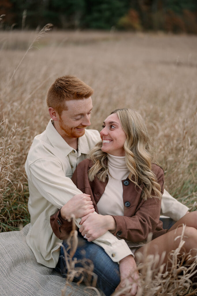 Couple embracing in a field during Michigan fall engagement session, natural tones and candid posing.