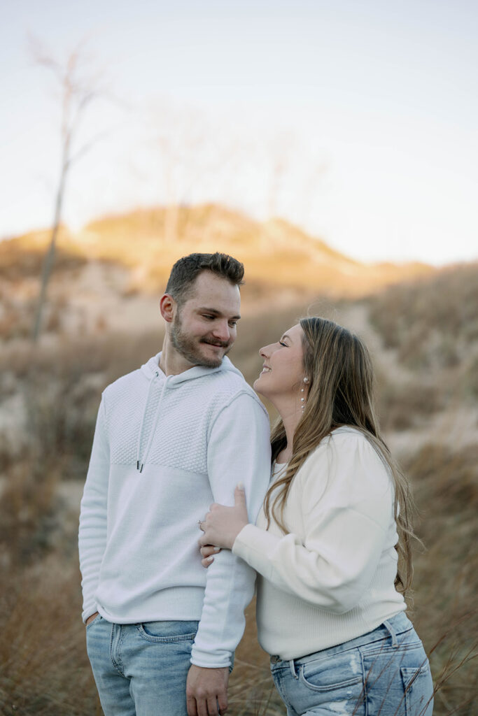 Close-up of couple smiling at Lake Michigan beach engagement session, warm sunset light.