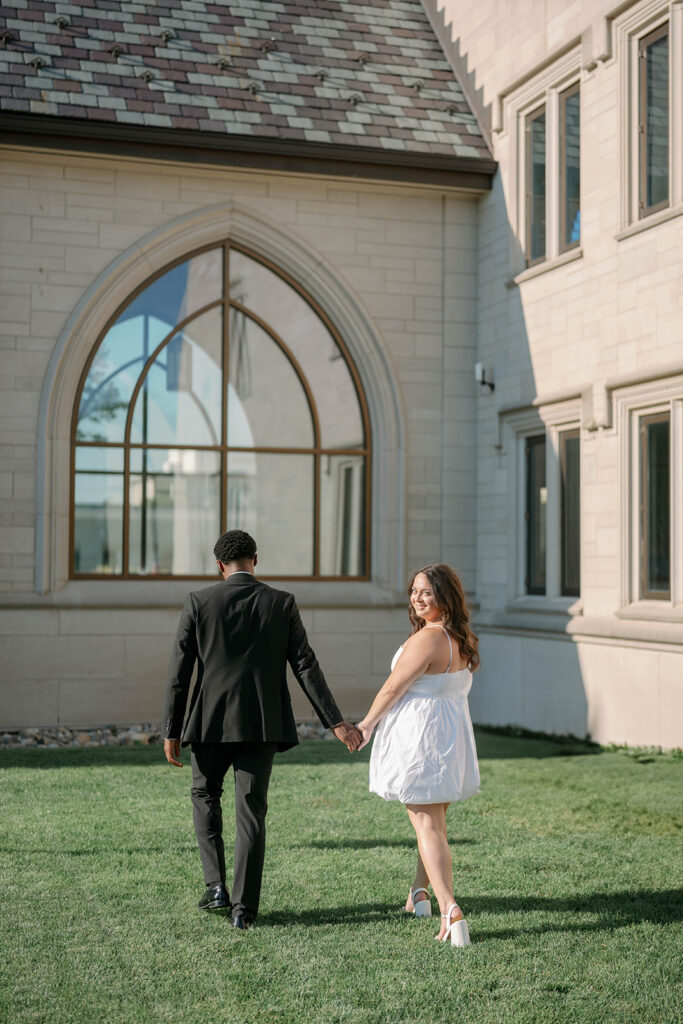 Couple walking near historic Kalamazoo building with arched windows, editorial city engagement photos in Michigan.