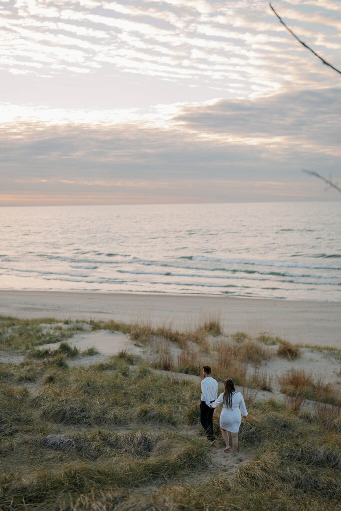 Couple standing together at Lake Michigan dunes during golden hour, natural and soft engagement photography.