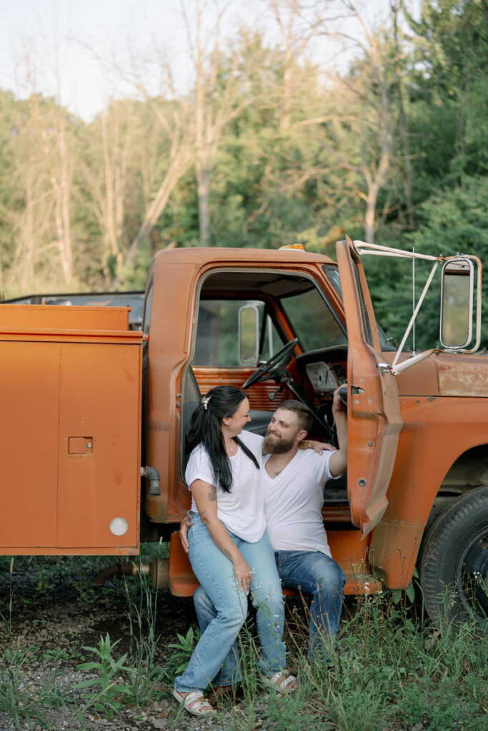 Couple sitting inside the open door of an orange vintage truck during their engagement style photography session