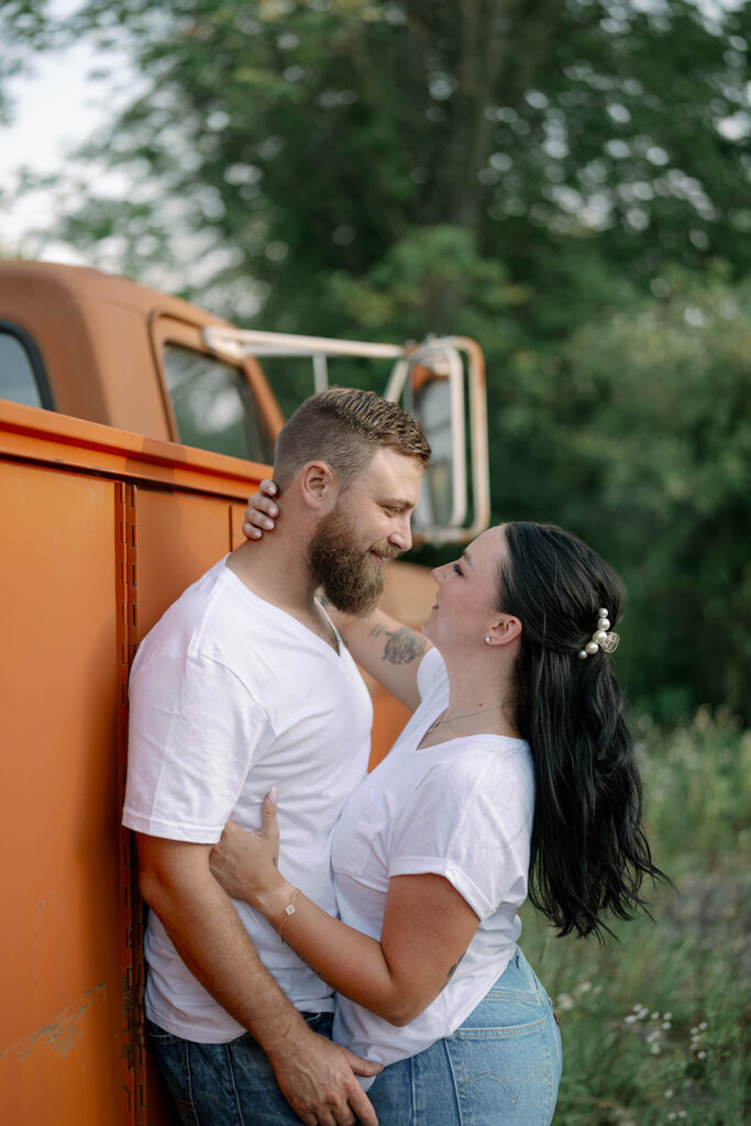Couple embracing beside an orange Jeep Wrangler during their Michigan engagement photos