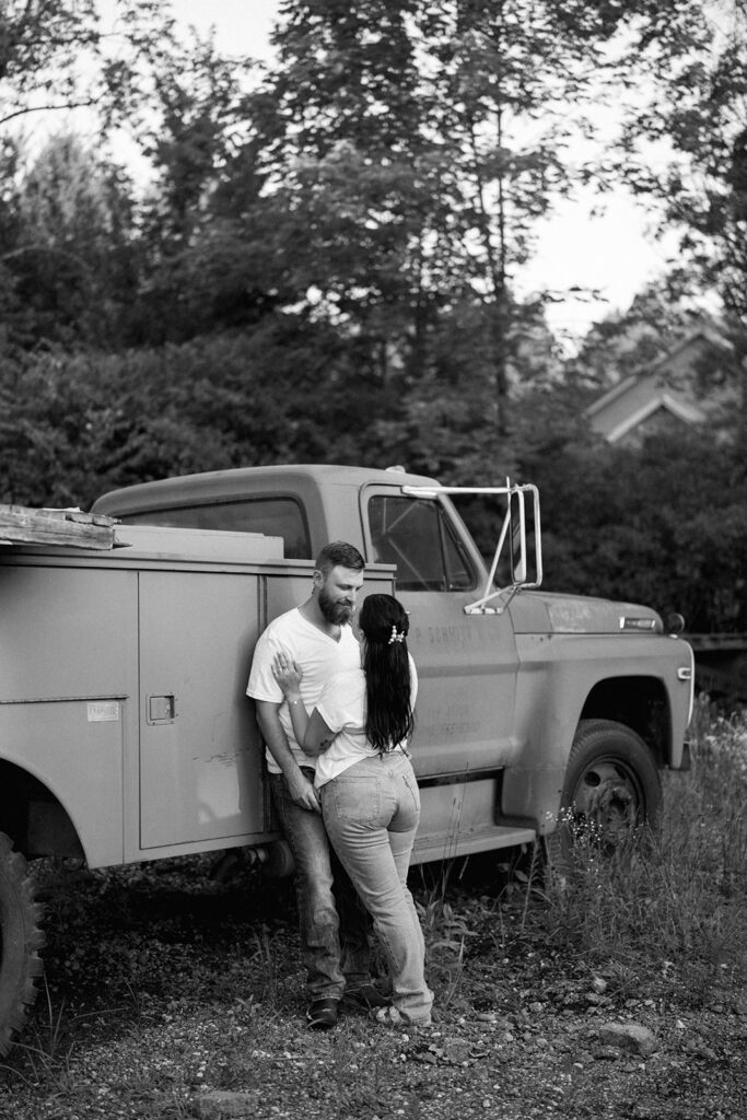 Black and white photo of couple standing beside a vintage truck during a candid outdoor photography session