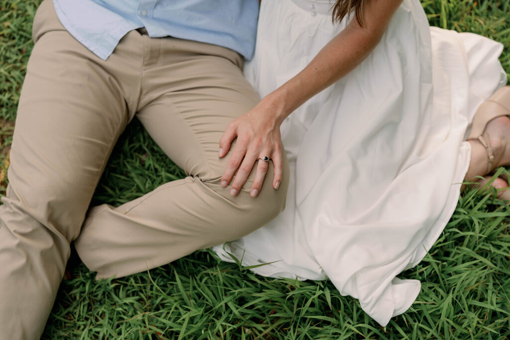 Couple sitting in the grass during their photography session with their hands resting together in a relaxed pose