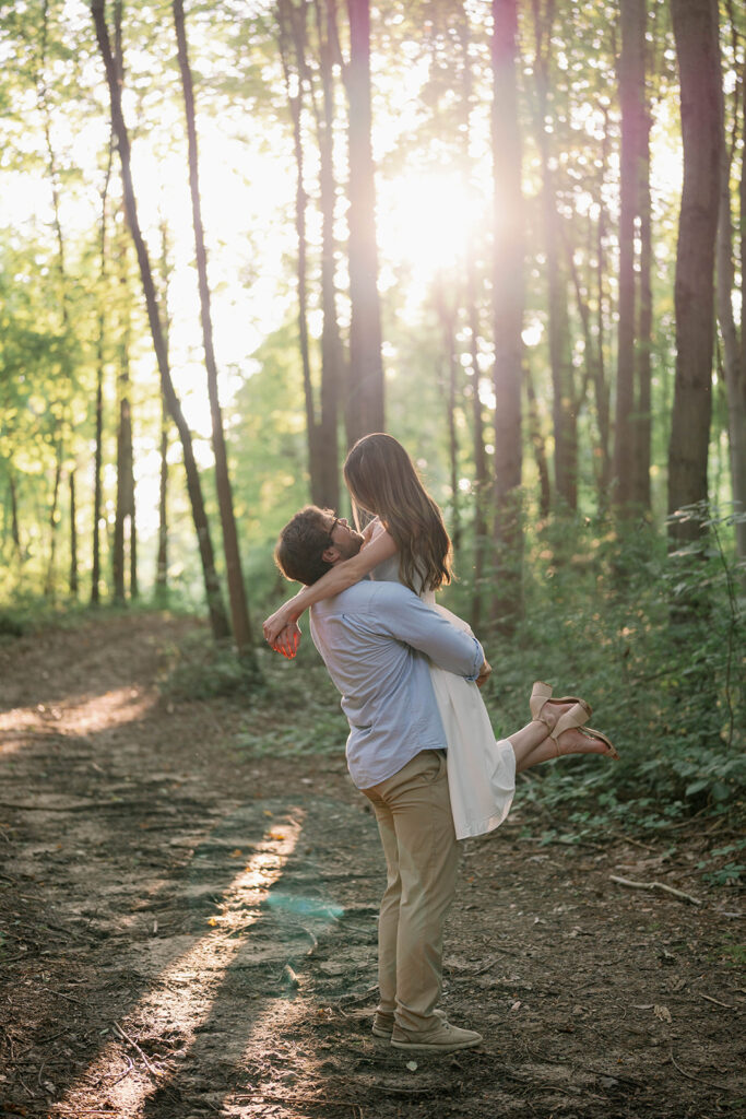 Partner lifting their loved one playfully while walking through a wooded path during their session