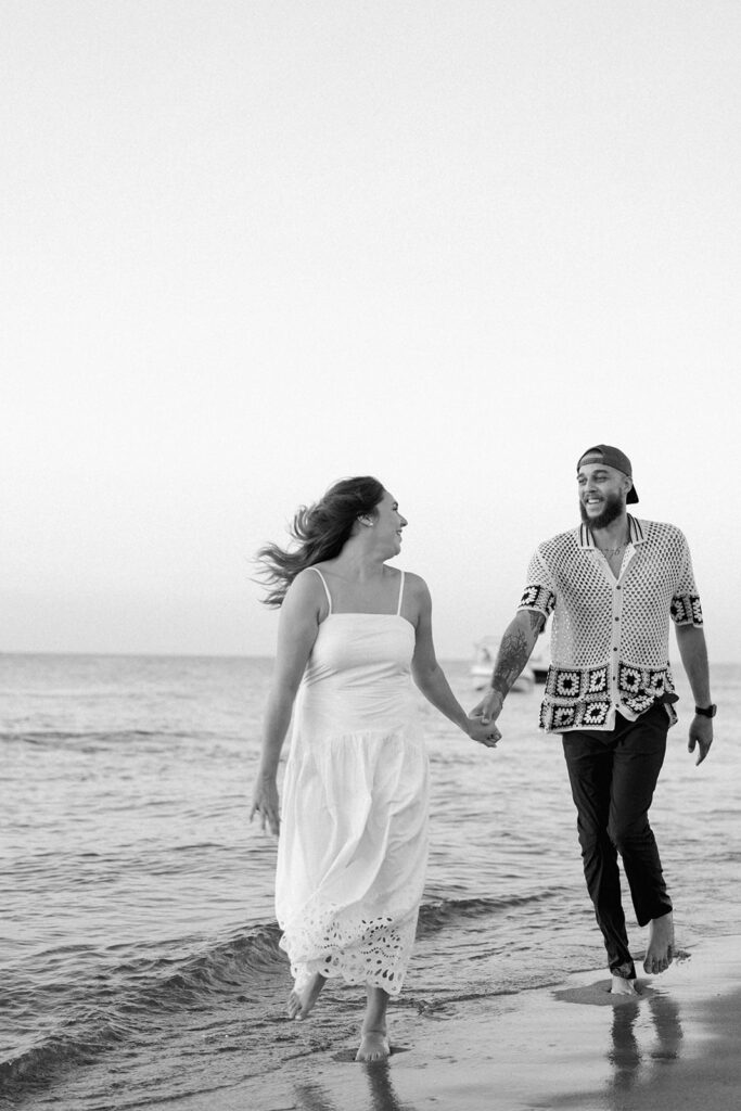 Couple running together at the edge of the water during a fun candid beach photography session