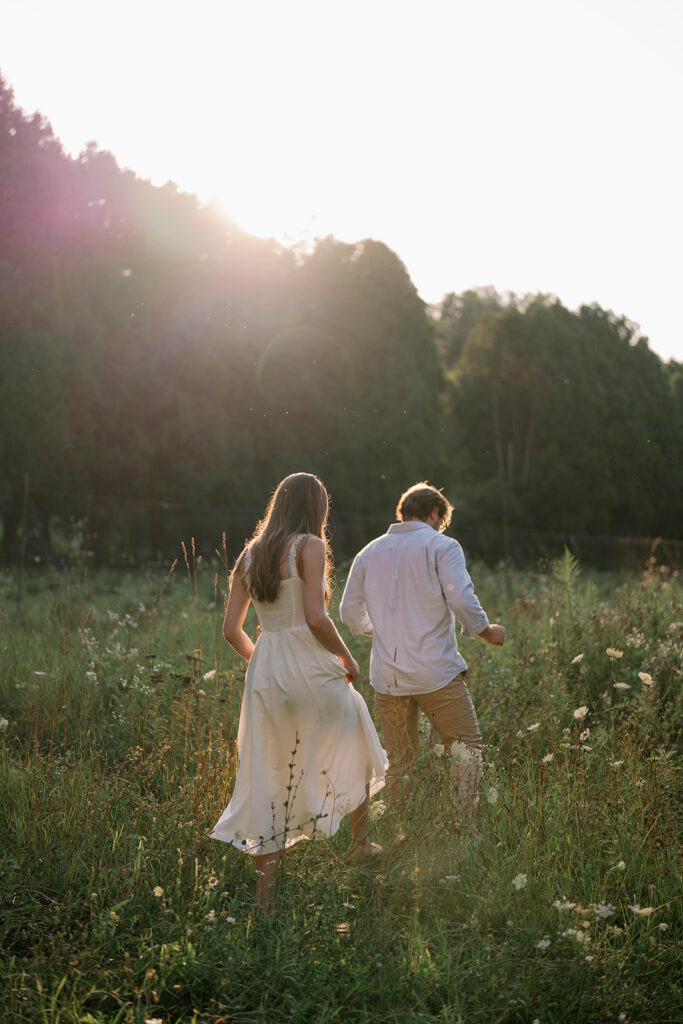 Couple walking through a sunlit field during their outdoor photography session at golden hour