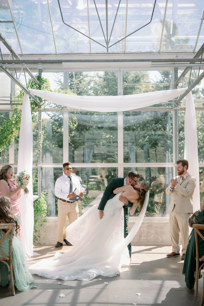 Couple sharing first kiss inside Ivy House greenhouse during a modern garden inspired wedding ceremony