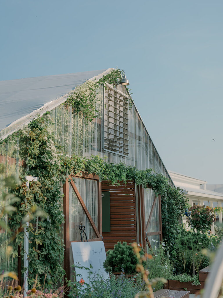 Greenhouse exterior at Of The Land in Battle Creek surrounded by lush greenery and natural outdoor setting