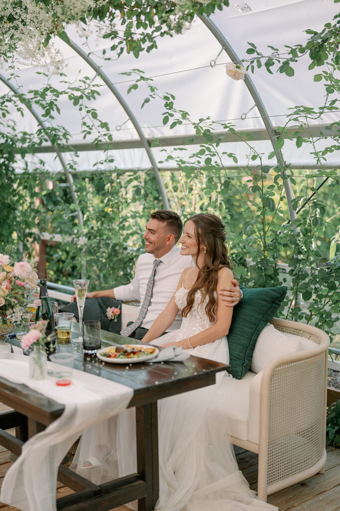 Couple sitting inside the greenhouse at Of The Land surrounded by vines and natural light during their outdoor Michigan wedding