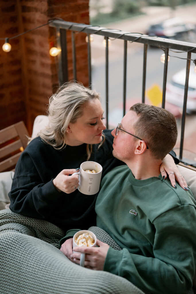 Couple sitting on balcony with coffee during cozy engagement session in Michigan