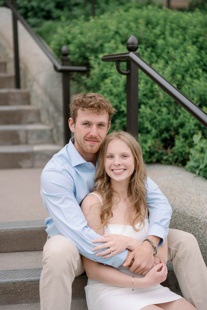 Engaged couple sitting on steps of historic building in Michigan, relaxed and natural portraits.