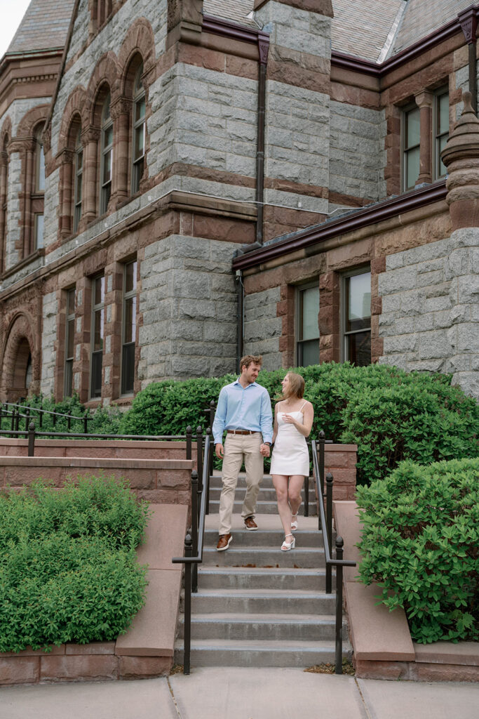 Engaged couple sitting on historic stone stairs during editorial Michigan engagement session, classic architecture background