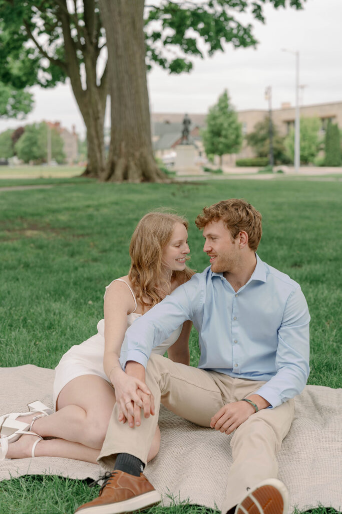 Couple sitting on blanket under tree on historic property during engagement session, soft and romantic moment.