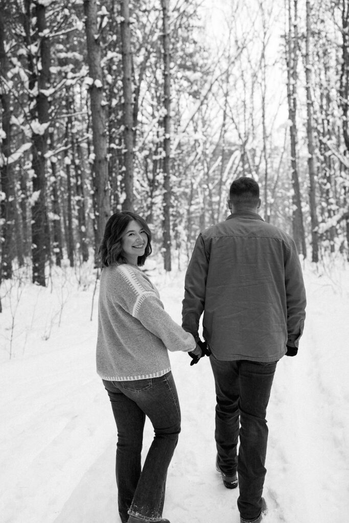 Couple walking hand in hand through a snowy forest at Al Sabo Land Preserve in Kalamazoo Michigan