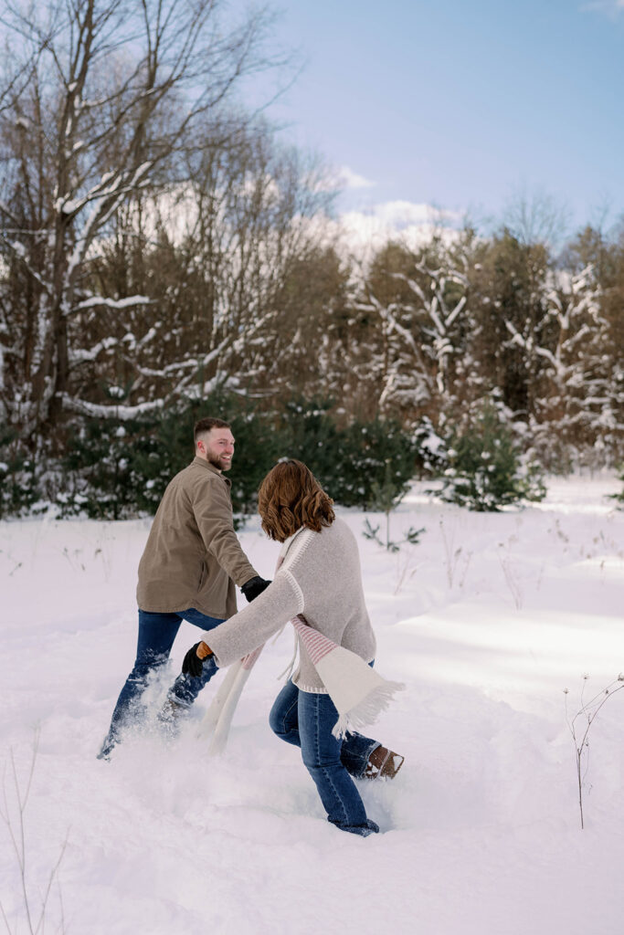 Couple running through deep snow during a playful winter couples session in Kalamazoo Michigan