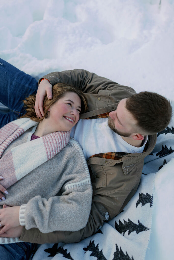 Color photo of a couple lying together on a blanket in the snow at Al Sabo Land Preserve