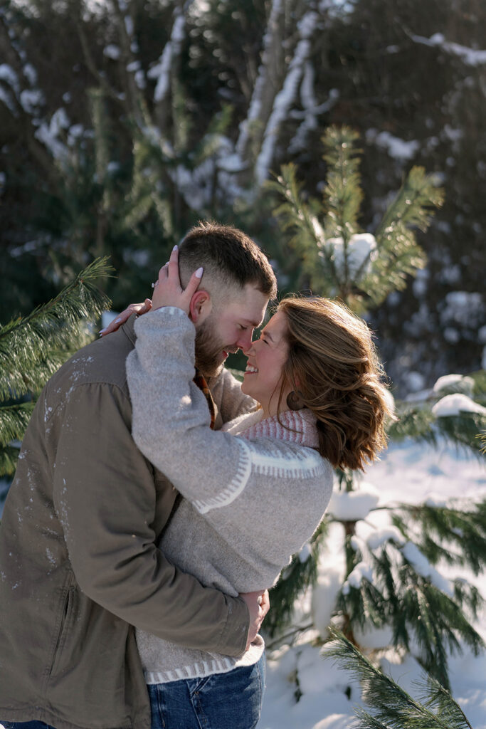 Couple embracing among snow covered evergreen trees during a winter engagement session in Southwest Michigan