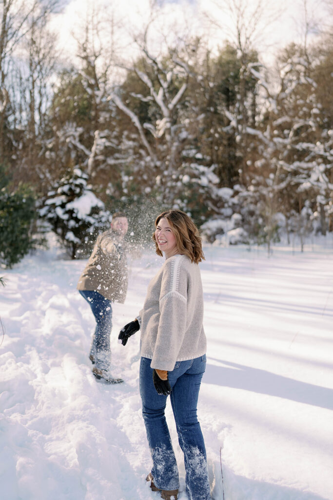 Color image of a woman laughing while standing in the snow during a winter couples session in Southwest Michigan