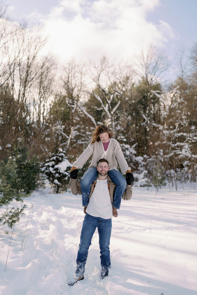 Couple piggybacking in the snow during a fun winter engagement session in Kalamazoo MI
