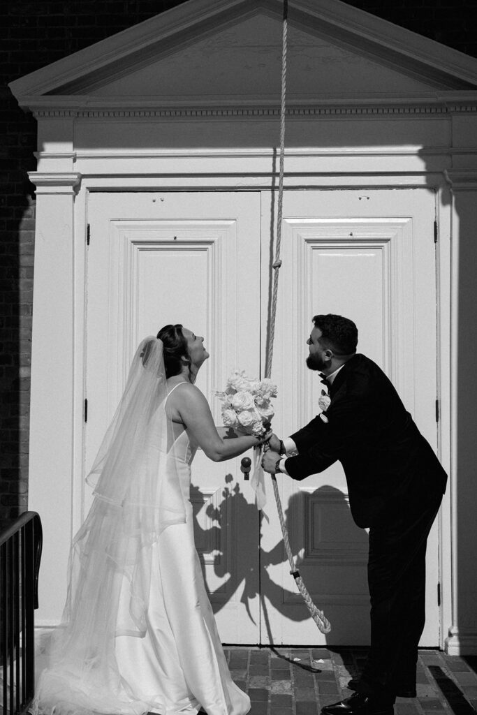 bride and groom ringing bell outside of chapel 
