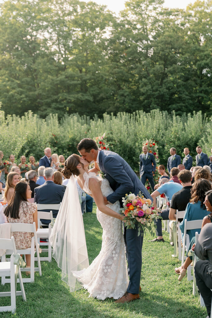 ride and groom kissing halfway down the aisle at Nugent Orchards wedding in Frankfort Michigan