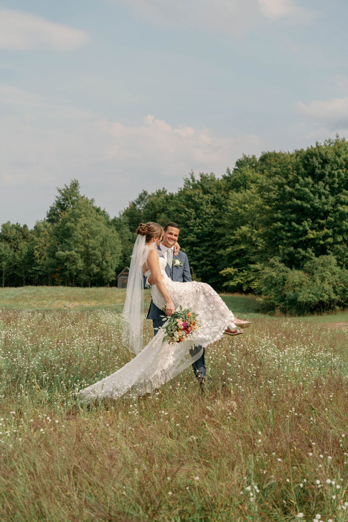 groom carrying bride through open field at Nugent Orchards wedding in Michigan