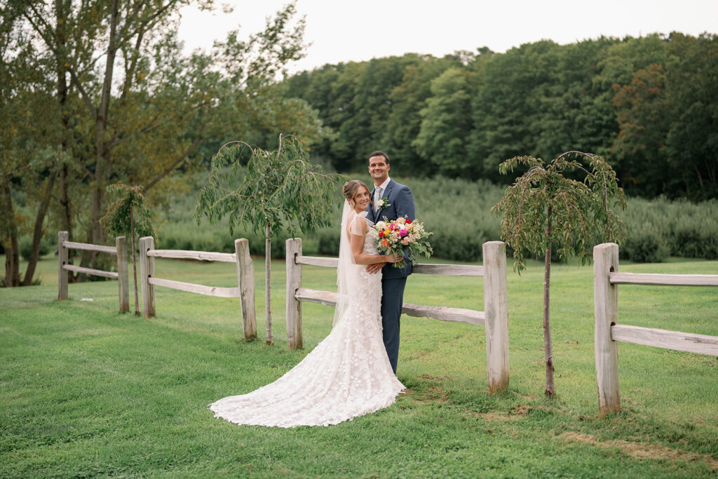couple standing by wooden fence at Frankfort Michigan orchard wedding