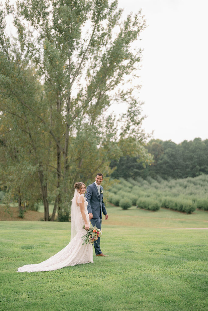 bride and groom walking together with orchard in background at Nugent Orchards wedding